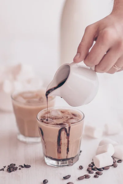 Light background. Iced coffee. Concept of a cooling drink. Marshmelow and coffee beans on the table. Summer drink. Cold coffee with milk and chocolate. Vertical shot.