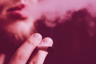 Bir adam elinde esrar, esrar ve çakmak tüttürür. Siyah arka planda sigara içmek. Tıbbi marihuana kullanımı ve esrar kullanımının yasallaştırılması kavramları. Siyah bir arkaplanda Violet boyası