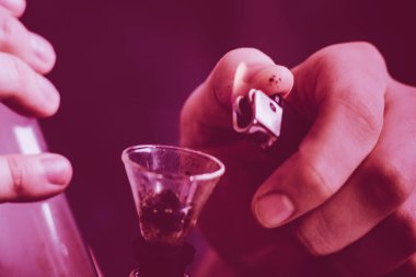 nargile ve onun elinde bir çakmak. Bir adam esrar ot, bir duman siyah bir zemin üzerine çekiyor. Tıbbi esrar kullanım ve yasallaştırma esrar kavramları. Menekşe renklendirme bir siyah arka plan üzerine