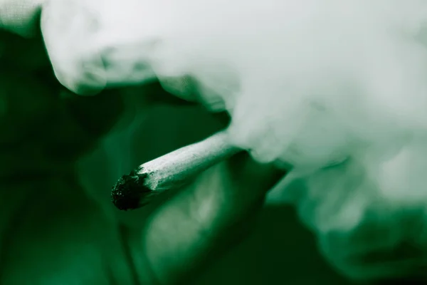 黑色背景下的烟雾。一个男人吸食大麻大麻, 一个关节和他手中的打火机。医疗用大麻的概念和大麻的合法化。在黑色背景绿色着色 — 图库照片