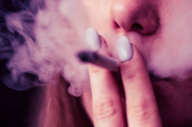 El A ortak bir esrar ot çekiyor. Siyah bir arka plan üzerinde duman. Tıbbi esrar kullanım ve yasallaştırma esrar kavramları. Pembe siyah bir arka plan renklendirme