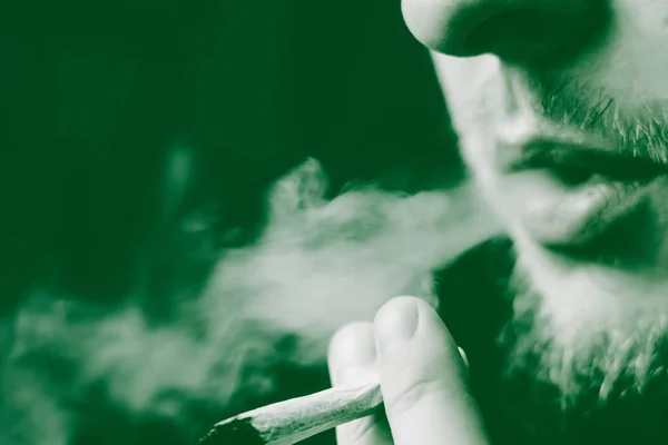 Articulación en mano de hombre. Un hombre fuma marihuana, una. Humo sobre fondo negro. Conceptos de uso médico de la marihuana y legalización del cannabis. Sobre un fondo negro —  Fotos de Stock