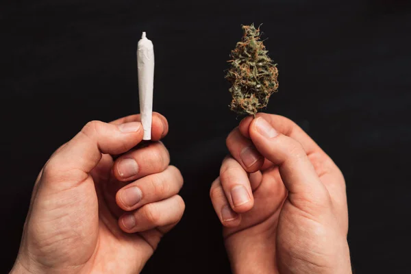 El concepto de consumo de marihuana. Sobre un fondo negro. top view Brote de cannabis y articulación en las manos de un hombre . —  Fotos de Stock