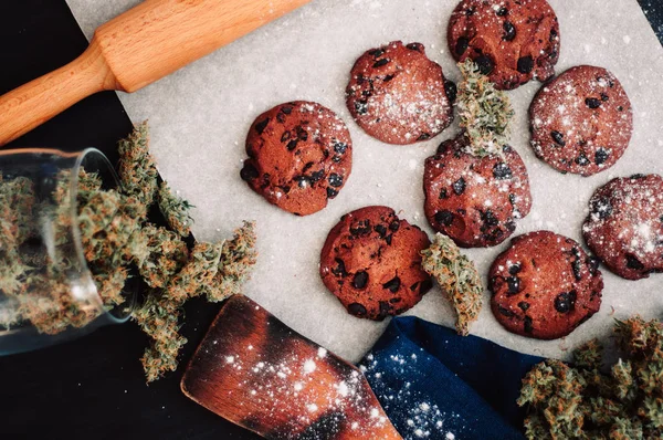 Godis med ogräs. Choklad cookies med marijuana. Godis med cannabis. Cannabis knoppar på en svart bakgrund. Bakning med tillägg av Cbd. ovanifrån — Stockfoto