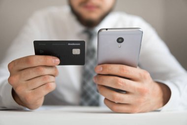 Akıllı telefon ve Internet ticareti. Genç işadamı onun elinde banka kredi kartıyla. Malların online ödeme. Online ödeme telefon aracılığıyla. Online Döviz Alım Satım ticaret.