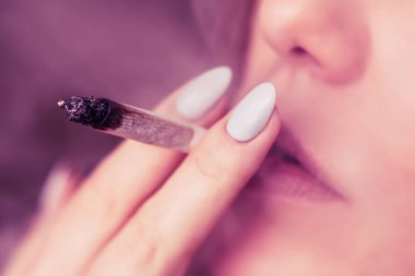 Esrar, elinde esrar Bir kadın sigara içiyor. Siyah arka planda sigara içmek. Tıbbi marihuana kullanımı ve esrar kullanımının yasallaştırılması kavramları. Siyah arka planda Pembe renklendirme