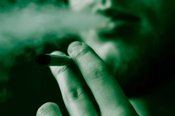Человек курит марихуану косяк и зажигалку в руках. Дым на черном фоне. Концепции использования медицинской марихуаны и легализации марихуаны. На черном фоне Зеленый оттенок — стоковое фото