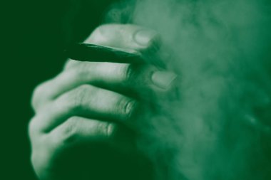 Bir adam sigara esrar esrar, esrar ve çakmak elinde. Siyah bir arka plan üzerinde duman. Tıbbi esrar kullanım ve yasallaştırma esrar kavramları. Siyah bir arka plan üzerinde yeşil renklendirme