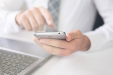 Bir dizüstü bilgisayar ile ofis işleri. Mali iş. Açık renkli. Akıllı telefon elinde tutuyor. Genç işadamı sakallı.