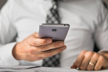 Akıllı telefon elinde tutuyor. İş adamı iş bilgisayar ile ofis işleri tablo. Genç işadamı sakallı. Mali iş. Açık renkli. Bir dizüstü bilgisayar ile ofis işleri.