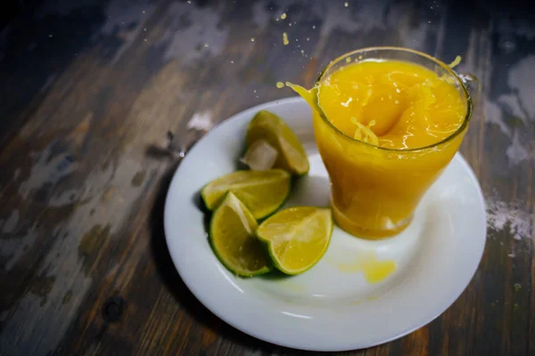 Un vaso de jugo de naranja con una gran salpicadura y lima en un plato — Foto de Stock