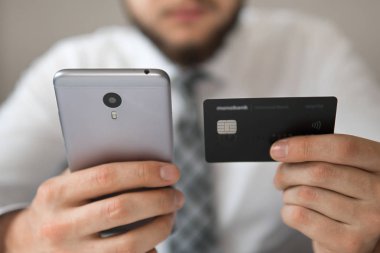 Genç işadamı onun elinde banka kredi kartıyla. Online ödeme telefon aracılığıyla. Malların online ödeme. Akıllı telefon ve Internet ticareti. Online Döviz Alım Satım ticaret.