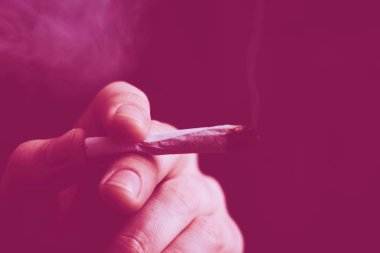 Bir adam elinde esrar, esrar ve çakmak tüttürür. Siyah arka planda sigara içmek. Tıbbi marihuana kullanımı ve esrar kullanımının yasallaştırılması kavramları. Siyah bir arkaplanda Violet boyası