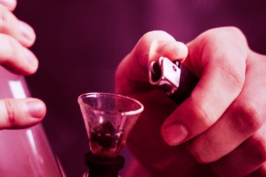 Bir adam elinde esrar, esrar ve çakmak tüttürür. Siyah arka planda sigara içmek. Tıbbi marihuana kullanımı ve esrar kullanımının yasallaştırılması kavramları. Siyah bir arkaplanda Violet boyası