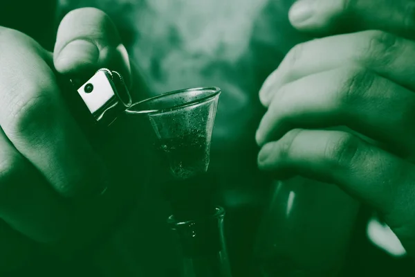 Bong och en tändare i handen. En man röker cannabis ogräs, rök på en svart bakgrund. Begreppet medicinsk marijuana användning och legalisering av cannabis. På en svart bakgrund grön färgning — Stockfoto