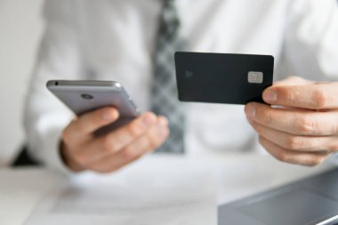 Akıllı telefon ve Internet ticareti. Malların online ödeme. Genç işadamı onun elinde banka kredi kartıyla. Online Döviz Alım Satım ticaret. Telefon aracılığıyla online ödeme.