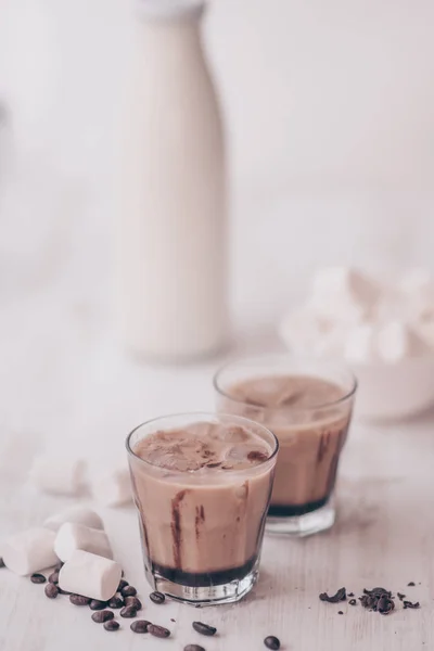 Marshmelow y granos de café en la mesa. Bebida de verano. Café frío con leche y chocolate. Disparo vertical. Fondo claro. Café helado. Concepto de bebida refrescante . — Foto de Stock