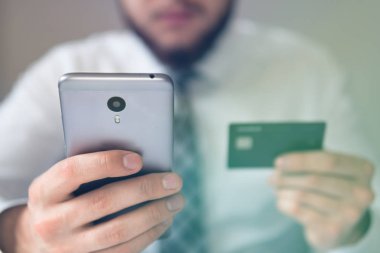 Akıllı telefon ve Internet ticareti. Online Döviz Alım Satım ticaret. Genç işadamı onun elinde banka kredi kartıyla. Malların online ödeme. Telefon aracılığıyla online ödeme.