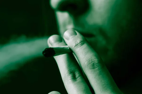 吸食大麻大麻, 一个关节和他手中的打火机。黑色背景下的烟雾。医疗用大麻的概念和大麻的合法化。在黑色背景绿色着色 — 图库照片