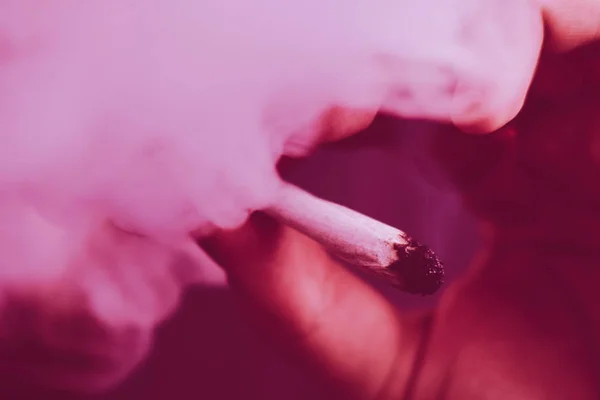 大麻杂草一个男人抽烟, 一个关节和打火机在他的手。在黑色背景上吸烟。医用大麻的概念和大麻合法化。在黑色背景紫罗兰色着色 — 图库照片