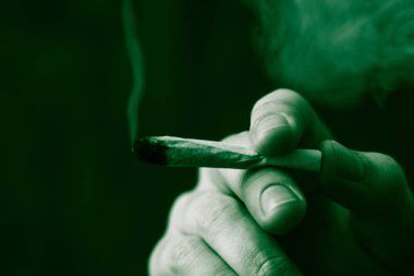 adam elinde ortak. Bir adam esrar ot çekiyor bir. Siyah bir arka plan üzerinde duman. Tıbbi esrar kullanım ve yasallaştırma esrar kavramları. Siyah bir arka plan üzerinde yeşil renklendirme