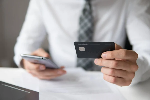 Un giovane uomo d'affari con una carta di credito in mano. Pagamento delle merci online. Negoziazione online sul cambio valuta. Smartphone e Internet Commerce. Pagamenti online tramite telefono . — Foto Stock