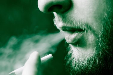 Bir adam sigara esrar esrar, esrar ve çakmak elinde. Siyah bir arka plan üzerinde duman. Tıbbi esrar kullanım ve yasallaştırma esrar kavramları. Siyah bir arka plan üzerinde yeşil renklendirme