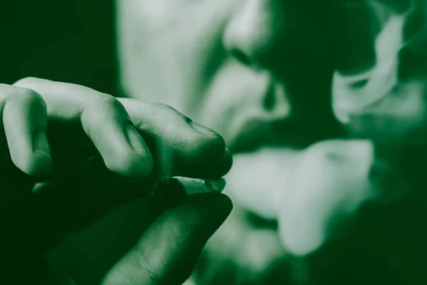 Un hombre fuma marihuana, un porro y un encendedor en sus manos. Humo sobre fondo negro. Conceptos de uso médico de la marihuana y legalización del cannabis. Sobre un fondo negro Tintado verde — Foto de Stock