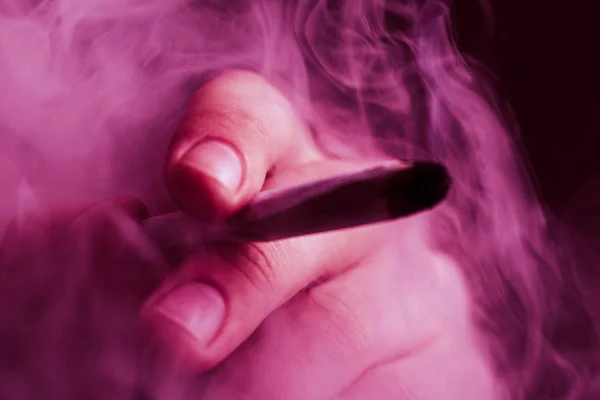 En man röker hasch, en joint och en tändare i sina händer. Rök på svart bakgrund. Begreppen medicinsk marijuana användning och legalisering av cannabis. På en svart bakgrund Violett toning — Stockfoto