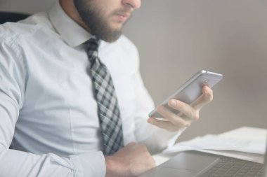 Smartphone elinde. Genç işadamı sakallı. İş adamı iş bilgisayar ile ofis işleri tablo. Mali iş. Açık renkli. Yakın çekim. Bir dizüstü bilgisayar ile ofis işleri.