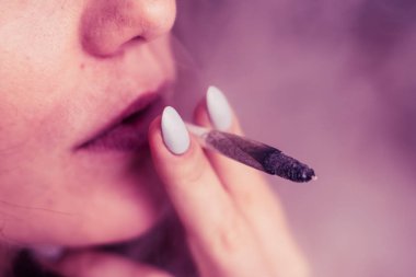 Esrar, elinde esrar Bir kadın sigara içiyor. Siyah arka planda sigara içmek. Tıbbi marihuana kullanımı ve esrar kullanımının yasallaştırılması kavramları. Siyah arka planda Pembe renklendirme