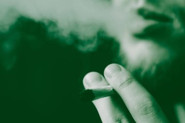 Bir adam sigara esrar esrar, esrar ve çakmak elinde. Siyah bir arka plan üzerinde duman. Tıbbi esrar kullanım ve yasallaştırma esrar kavramları. Siyah bir arka plan üzerinde yeşil renklendirme