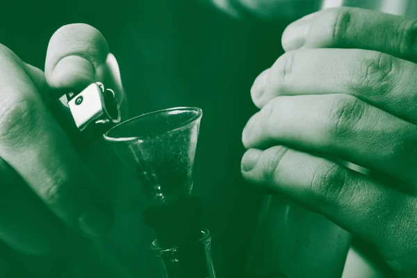 En man röker bong cannabis ogräs. Rök på en svart bakgrund. Begreppet medicinsk marijuana användning och legalisering av cannabis. På en svart bakgrund grön färgning — Stockfoto