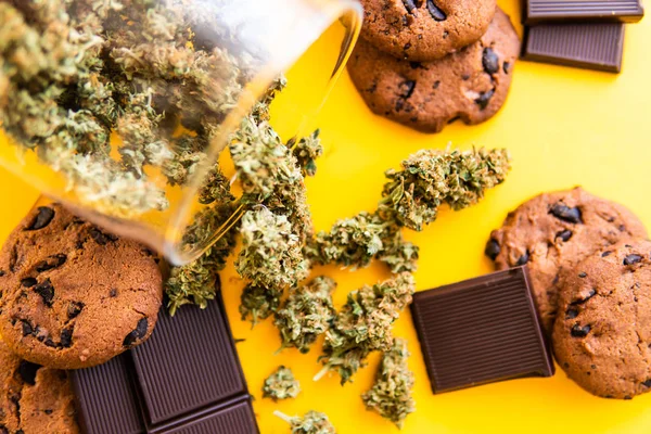 Cannabis CBD erva Chocolate e bolachas. Tratamento de maconha medicinal para uso em alimentos, fundo amarelo. Biscoitos e Chocolate com maconha e botões de maconha na mesa . — Fotografia de Stock