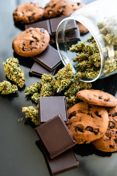 Csokoládé és a cookie-kat, a kannabisz és a rügyek, a marihuána, az asztalon. Kezelés orvosi marihuána használata az élelmiszer-, a fekete háttér. Cookie-k és a kannabisznövény Cbd csokoládé. — Stock Fotó