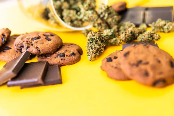 Cannabis CBD kruid Chocolade en koekjes. Behandeling van medicinale marihuana voor gebruik in voedsel, gele achtergrond. Koekjes en chocolade met wiet en knoppen van marihuana op tafel. — Stockfoto