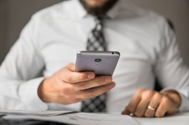 Genç işadamı Holding smartphone el sakallı. Bir dizüstü bilgisayar ile ofis işleri. İş adamı iş bilgisayar ile ofis işleri tablo. Mali iş. Açık renkli.