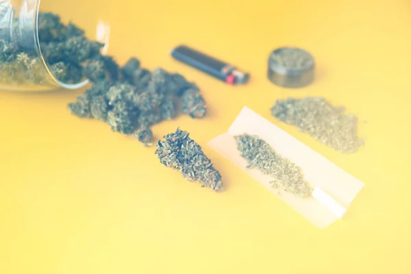 Blunt and Lighters. Hemp legalisation. Herb grinder Fresh marihuana. CBD and THC on buds in cannabis. Cannabis buds in hand on yellow background Background for Copy space. Top view. light leaks — Stock Photo, Image
