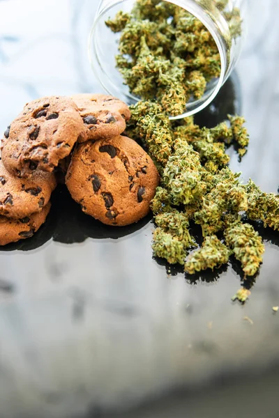 Conceito de cozinhar com erva de cannabis. Tratamento de maconha medicinal para uso em alimentos, fundo preto. Biscoitos com maconha e botões de maconha na mesa. Tiro vertical — Fotografia de Stock