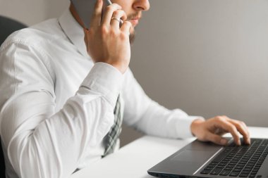 İş adamı iş bilgisayar ile ofis işleri tablo. Akıllı telefon elinde tutuyor. Bir dizüstü bilgisayar ile ofis işleri. Mali iş. Genç işadamı sakallı. Açık renkli.