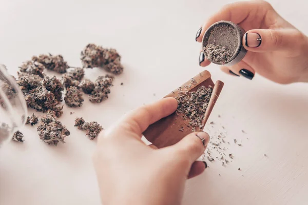 Cierre de marihuana roma con molinillo. Concepto de consumo de cannabis. Mujer preparando y rodando marihuana marihuana conjunta. Mujer rodando un porro de marihuana sobre fondo blanco . — Foto de Stock