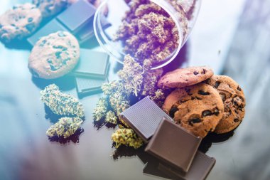Kurabiye ve CBD otlu çikolata kavramı. Yiyecek ve siyah arka planda tıbbi marihuana kullanımı. Çikolata ve kurabiyeler, masada esrar ve esrar tomurcukları..