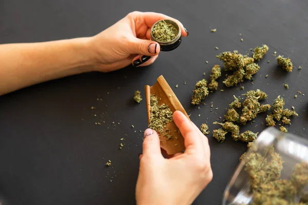 Donna che prepara e arrotola marijuana cannabis comune. Concetto di utilizzo della pentola. Chiudi Donna che rotola una canna di marijuana. Primo piano di marijuana smussata con grinder . — Foto Stock