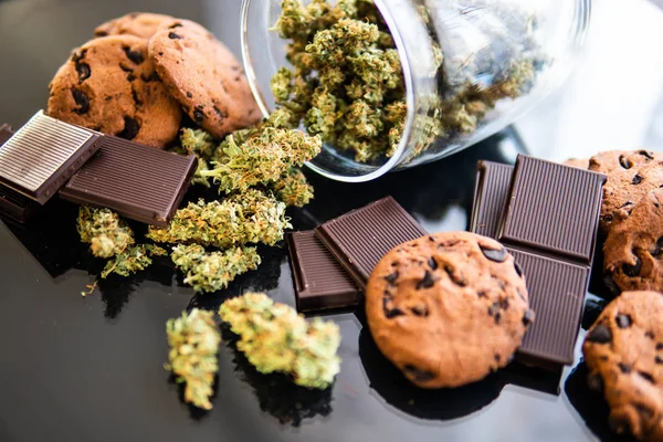 Treatment of medical marijuana for use in food, black background. Concept of Cookies and chocolate with cannabis herb CBD. Chocolate and Cookies with cannabis and buds of marijuana on the table. — Stock Photo, Image