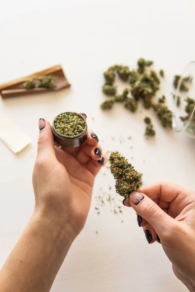 A marihuána köszörűs közelsége. a marihuána használatának koncepciója. Egy nő kannabiszt gurít fehér háttérrel. Nő előkészítő és gördülő marihuána cannabis joint. — Stock Fotó