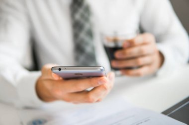 Akıllı telefon elinde tutuyor. Genç işadamı sakallı. Bir dizüstü bilgisayar ile ofis işleri. Açık renkli. Mali iş. Bilgisayarda ofis işleri tabloda ile işadamı çalışma.