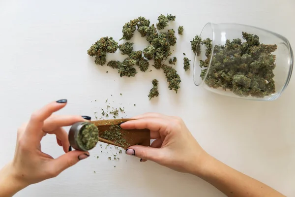 Concept de consommation de marijuana. Gros plan de marijuana émoussée avec broyeur. Femme préparant et roulant cannabis joint. Femme roulant un joint de marijuana sur fond blanc. Vue du dessus — Photo