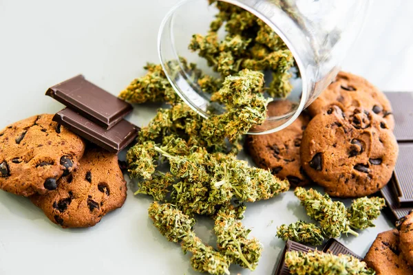 Tratamiento de la marihuana medicinal para uso en alimentos, fondo blanco. Galletas con hierba de cannabis CBD. Galletas con cannabis y cogollos de marihuana sobre la mesa . — Foto de Stock