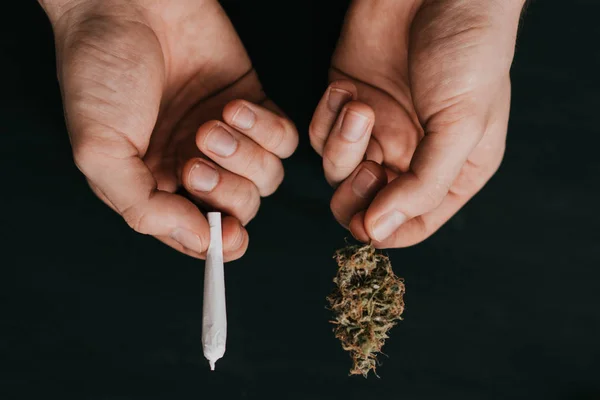 Sobre un fondo negro. top view Brote de cannabis y articulación en las manos de un hombre. El concepto de consumo de marihuana . — Foto de Stock