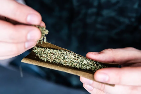 Concepção de narcóticos. Um homem a enrolar marijuana. Homem preparando e enrolando maconha cannabis Blunt. Fecha. Close up de viciado acendendo maconha Blunt com isqueiro . — Fotografia de Stock